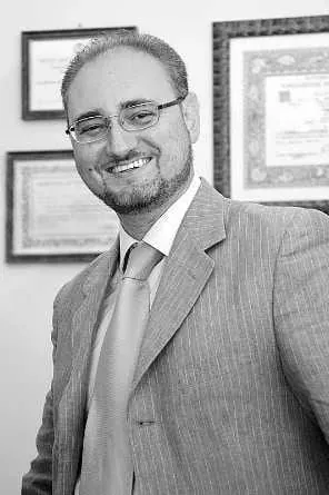 Foto ritratto dell'avvocato Maurilio Marangio. La foto è in bianco e nero e lo ritrae in piedi, a mezzo busto, mentre sorride in giacca e cravatta, indossando gli occhiali.